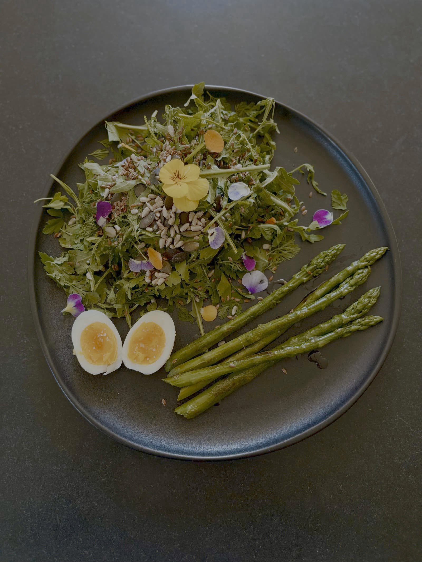 Assiette de saison de la table d'hôte d'été : salade de jeunes pousses, fleurs comestibles, œuf mollet et asperges
